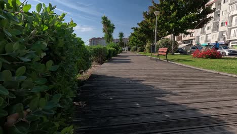 Wooden-street-sidewalk-with-plants-and-garden-on-the-sides-in-front-of-the-village-houses-and-people-going-about-their-daily-lives-in-summer-with-sunny-day