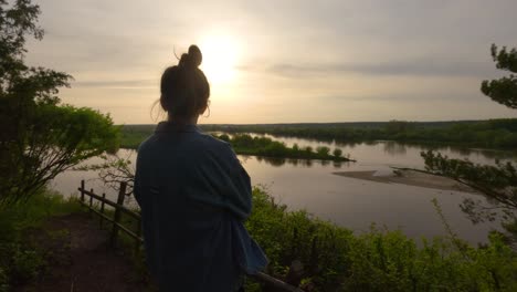 Lady-contemplates-sunset-in-quiet-delta-river-landscape-as-seen-from-behind-natural-reservoir,-tranquil-atmosphere-in-Polish-countryside