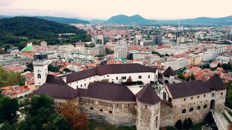 Aerial-pan-shot-of-Ljubljana-castle-in-Slovenia,-showing-the-contrast-of-the-Old-Town-with-the-modern-skyline-of-the-capital
