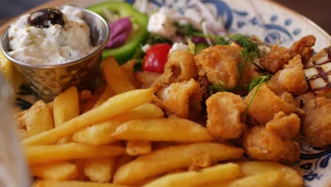 Fork-picks-feta-cheese,-tzatziki-and-fries-from-plate-of-Greek-food