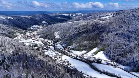 Drone-slow-fly-in-the-Meurthe-valley,-Habeaurupt,-in-Plainfaing-with-snow-covered-landscape-during-springtime-with-blue-sky-and-big-clouds