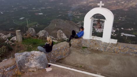 Hiker-Girls-Sit-on-Mountain-Top-and-Enjoys-Epic-360-Degree-Viewpoint-High-Above-Cliff--Greek-Island-of-Crete