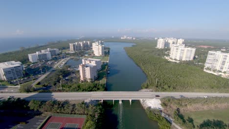Aerial-4K-Drone-footage-of-along-the-Vanderbilt-Channel-and-over-cars-driving-along-Bluebill-Avenue-bridge-back-and-forward-to-Wiggin-Pass-Beach-in-Naples,-Florida,-USA