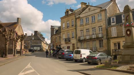 Historical-town-center-of-Clecy-with-houses,-parked-cars-and-memorial