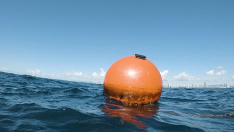 Large-orange-buoy-marking-a-new-artificial-reef-close-to-a-city-skyline-moves-about-with-the-ocean-swell