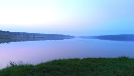 Morgens-Ruhiger-See,-Vor-Sonnenaufgang-Spiegelt-Sich-Der-See-In-Den-Atmosphärischen-Effekten-Des-Himmels-Und-Ist-Von-Nebligen-Nebeln-Umgeben