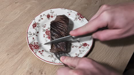 Cutting-well-done-fillet-steak-using-knife-and-fork-on-the-kitchen-plate