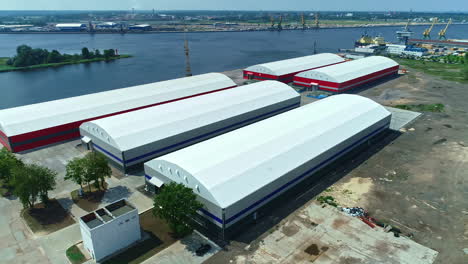 Warehouses-with-white-Long-Roofs-establishing,-Maritime-Port-Coastal-Drone-Shot
