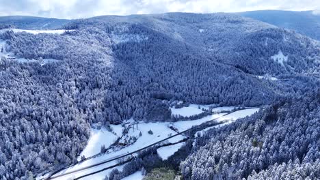 Drone-slow-yawing-fly-in-a-mountain-valley-covered-with-snow-during-springtime-with-blue-sky-and-big-clouds