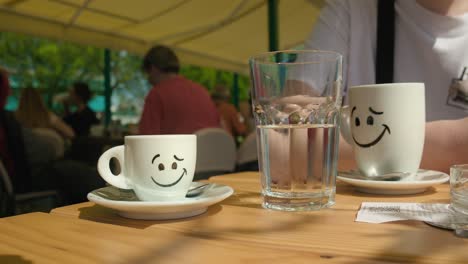Fröhliche-Kaffeetassen-Mit-Einem-Klaren-Wasserglas-Auf-Einem-Cafétisch