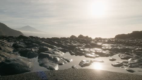 Morgenstrand-Mit-Schwarzem-Sand,-Felsen-Und-Sonnenreflexion-In-Gezeitentümpeln,-Playa-De-La-Arena,-Kanarische-Inseln,-Teneriffa,-Vertikale-Schwenk