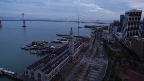 San-Francisco-CA-USA,-Aerial-View-of-Ferry-Building,-Embarcadero-Traffic,-Piers-and-Oakland-Bridge-in-Twilight