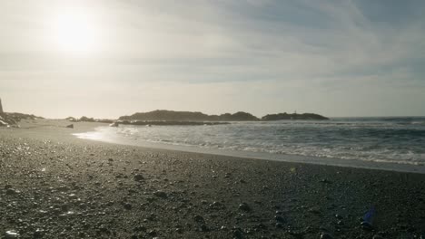 Teneriffa-Schwarzer-Sandstrand-Kieselsteine-Sonnenreflexion-Entlang-Der-Küste-Klarer-Himmel-Niedriger-Winkel,-Kanarische-Inseln