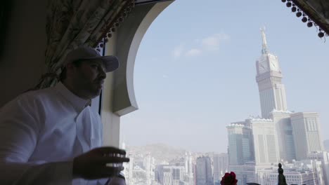 Man-Drinking-And-Having-Conversation-At-Restaurant-With-View-of-The-Clock-Towers-In-Mecca,-Saudi-Arabia