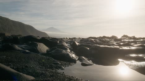 Ethereal-Tenerife-beach-at-dawn-with-black-sand-and-volcanic-rock-and-misty-Pico-del-Teide-in-the-background,-Playa-de-la-Arena-Canary-Islands