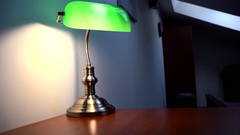 Green-Reading-Lamp,-glowing-with-a-yellow-light-on-the-brown-desk