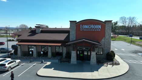 Customer-entering-and-leaving-famous-Longhorn-Steakhouse-during-sunny-day-in-American-Suburb