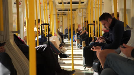 Static-angle-of-commuters-sitting-aboard-a-moving-London-overground-train,-suitcases-in-tow,-as-the-train-curves-and-sunlight-fades