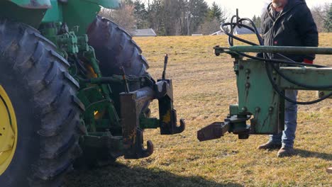 Farmer-attaching-a-plow-to-the-3-point-hitch-on-the-rear-of-tractor,-hydraulic-hoses-are-visible-but-not-connected