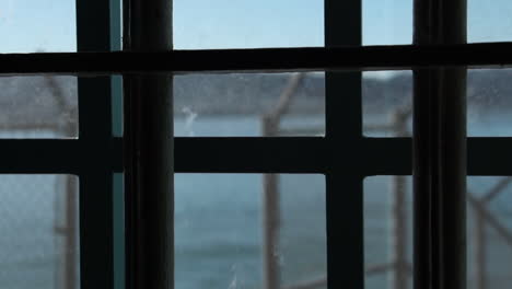 Alcatraz-Gefängnis-Detail,-Fenster-Mit-Metallstangen-Und-Hoher-Zaun-Mit-Stacheldraht