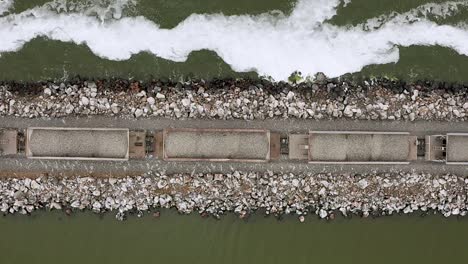 Freight-train-transports-stone-by-wavy-water,-rising-top-down-aerial