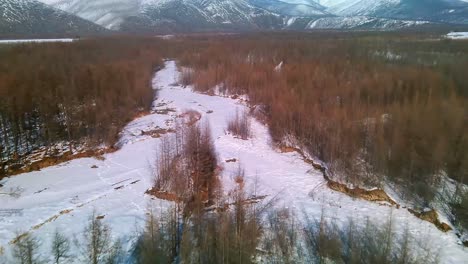 Volando-Sobre-Un-Río-Helado-Y-Un-Bosque-Gris-En-La-Soleada-Yakutia-4k