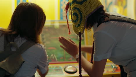 Rearview-of-girl-in-knitted-headwear-hitting-button-at-carnival-game-with-friend
