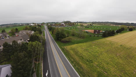 FPV-drone-over-intersection-in-rural-area-of-Pennsylvania,-arriving-amateur-Baseball-field-during-grey-sky