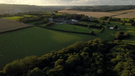 Drone-flies-towards-farm-in-Cornwall,-UK-at-sunset