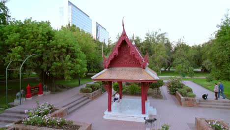 Menschen,-Die-Mit-Ihren-Hunden-Auf-Der-Thailand-Plaza-Spazieren-Gehen,-Denkmal-Im-Araucano-Park,-Aufsteigende-Luftaufnahme,-Santiago-De-Chile