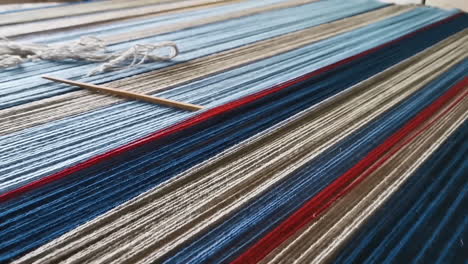 Multicolor-wool-threads-in-closeup-on-a-weaving-board-with-weaving-needle,-pan-left