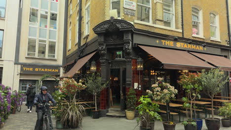 El-Hombre-Baja-El-Toldo-En-El-Pub-Starman,-Pasa-Un-Mensajero-En-Bicicleta,-Heddon-Street,-Londres,-Día.