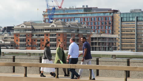 Two-pedestrians-walking-along-London-Bridge,-framed-by-the-city's-towering-buildings-in-the-backdrop