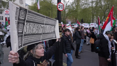 A-person-holds-a-black-and-white-banner-that-reads,-“Stop-Arming-Israel”-during-a-protest-on-Parliament-Square