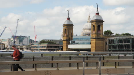 A-man-walking-on-London-Bridge,-pushing-a-suitcase-while-holding-a-phone,-tracked-by-a-gimbal