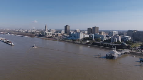 Weite-Luftaufnahmen-Der-Innenstadt-Von-Baton-Rouge-über-Dem-Mississippi-River-Mit-Einem-Schlepper,-Der-Auf-Eine-Gruppe-Von-Lastkähnen-Zusteuert