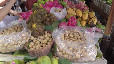 An-Asian-lady-purchases-a-variety-of-tropical-fruits-langsat,-duku,-salak,-mango,-apple,-orange-dragon-fruits-at-the-asian-wet-traditional-fruit-market-in-indonesia