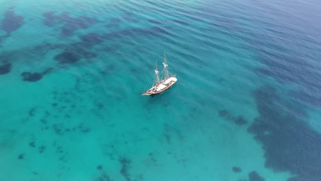 Velero-De-Madera-En-Un-Mar-Azul-Claro-En-Las-Cícladas,-Grecia,-Vista-Aérea-De-Drones