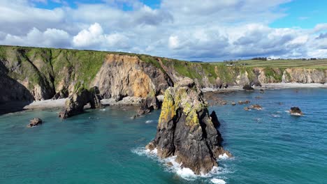 Drone-circling-jagged-sea-stacks-with-waves-dramatic-rock-formations-and-sea-caves-on-headland-Waterford-Coast-Ireland-impressive-nature-in-a-stunning-location