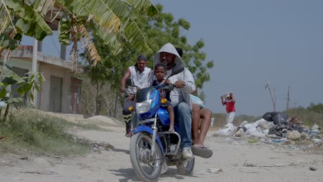 Una-Mujer,-Un-Hombre-Y-Un-Niño-Recorren-Sus-Motocicletas-Por-Un-Barrio-Pobre-Bajo-El-Sol.