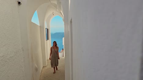 Una-Mujer-Camina-Por-Un-Estrecho-Callejón-Entre-Casas-En-La-Isla-Griega-De-Santorini