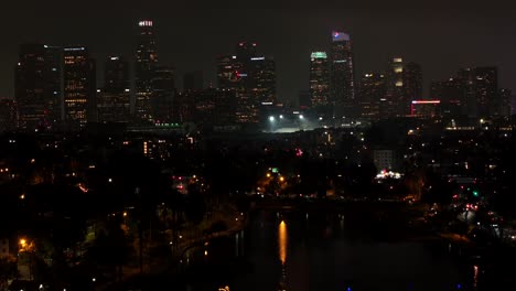 Aerial-rising-above-downtown-Los-Angeles-on-a-dark-night,-Echo-Park-with-lake-in-foreground