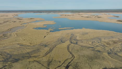 Aerial-establishing-view-of-the-lake-overgrown-with-dry-reeds,-lake-Pape-nature-park-,-sunny-spring-day,-reflections-on-the-water-surface,-wide-drone-shot-moving-forward