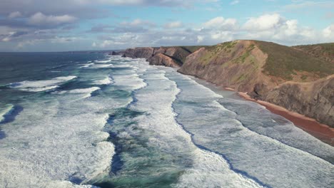 Aerial-4k-drone-establishing-shot-of-heavy-waves-at-praia-da-Cordoama-hidden-cliff-coastline-near-the-Algarve-region-of-Portugal