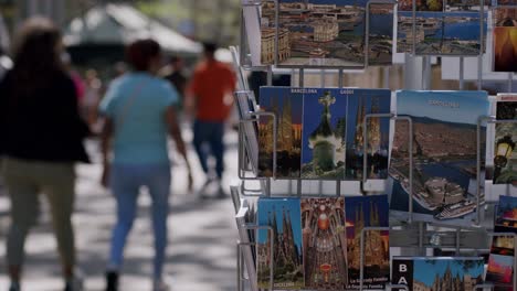 Touristen,-Die-An-Einem-Sonnigen-Tag-Postkarten-Mit-Sehenswürdigkeiten-Von-Barcelona-Durchstöbern,-Geringer-Fokus