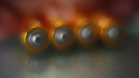 Macro-video-of-a-pile-of-rolling-batteries-on-a-desk-with-reflection,-golden-battery,-slow-motion-120-fps,-Full-HD,-push-in-smooth-movement