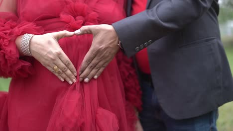 Closeup-shot-of-a-couple-posing-and-making-heart-in-belly-for-maternity-photoshoot