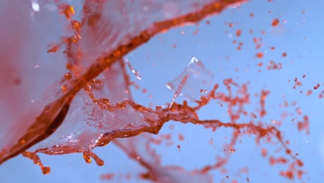 Slow-motion-footage-captures-a-wine-glass-shattering-against-a-blue-backdrop,-portraying-the-broken-glass-effect-with-artistic-flair
