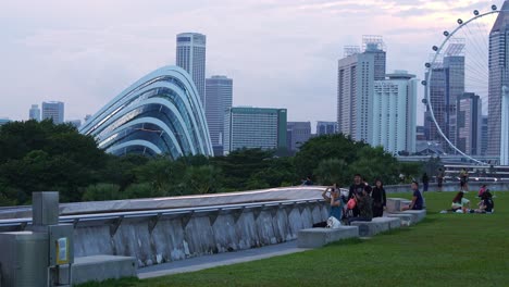 Marina-Barrage,-Stadtpark-Auf-Dem-Dach,-Statische-Aufnahme-Von-Menschen-Beim-Picknick-Und-Abhängen-Auf-Dem-Grünen-Rasen-Mit-Dem-Riesenrad-Singapore-Flyer-Und-Den-Gärten-An-Der-Bucht-Im-Hintergrund