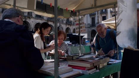 People-browsing-books-at-an-outdoor-market-in-Barcelona,-sunny-day
